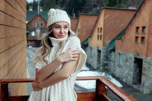 Portrait of a beautiful girl in a white hat and sweater on the street on the balcony. Warm winter clothes.