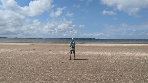 adult man with grey hair standing on the beach and looking over the water