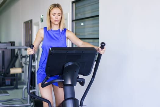 Fit serious caucasian woman on elliptical trainer at gym