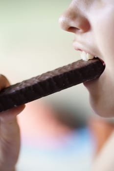 Side view of crop unrecognizable young girl eating chocolate protein bar at home