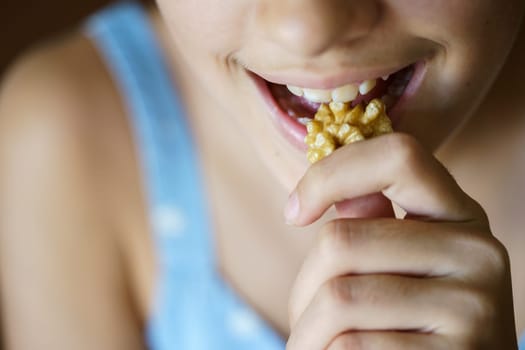 From above closeup of crop unrecognizable teenage girl eating healthy walnut kernel at home