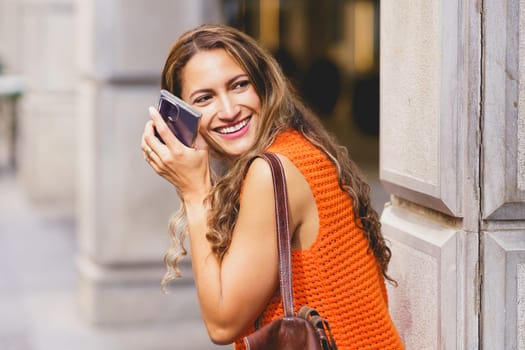 Happy shy latin beauty woman with mobile phone smiling in the city