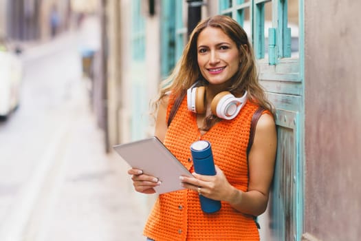 Latin happy woman holding reusable water bottle while using digital tablet in the city