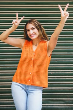 Vertical photo of a happy latin woman gesturing victory with fingers and smiling