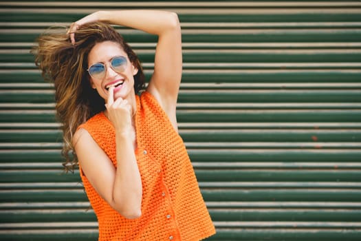 Urban portrait of a cool latin woman with finger on mouth smiling at camera holding her hair