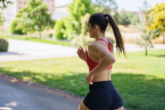 In the park, a woman in a red sports bra and black shorts is jogging with determination, demonstrating dedication to fitness and commitment to her workout routine. She embodies an active lifestyle