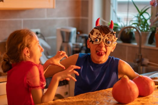brother and sister showing scary faces while decorating house with Halloween decor, Caucasian girl in devil costume, teenage boy in ghost glasses playing in darkened room, traditional autumn holiday