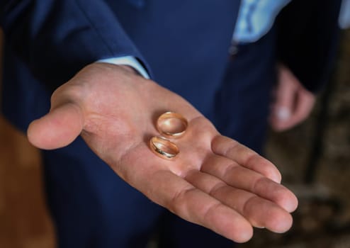 The groom's hand in the palm of his hand holds two gold wedding rings in close-up.