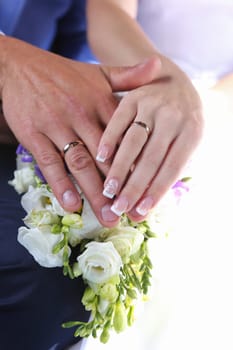 The bride's hand with the wedding ring lies on the hand of the groom, wedding bouquet.