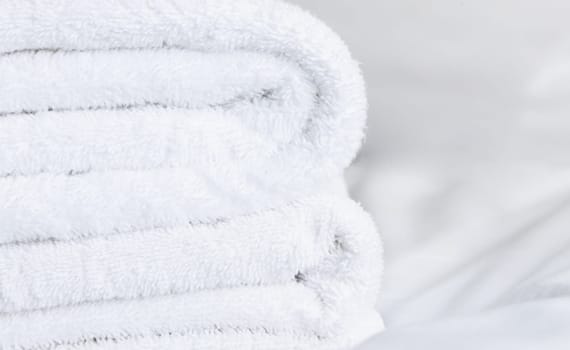 White terry towels stacked on top of each other lie on a white sheet close-up.
