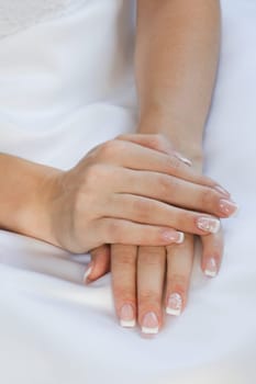 Beautiful young hands lying on a light colored wedding dress, hand on hand. Wedding manicure.