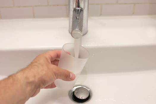 A man's hand pours water from a tap. Water flows from the tap into a glass.