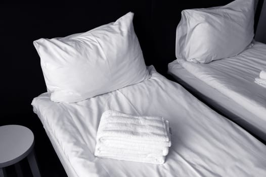 Freshly made beds with white sheets, white pillows, and towels. Fragment of a cozy bedroom.