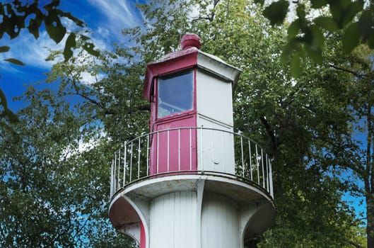 Low angle view of a lighthouse. The upper part of the lighthouse white and red, the window, against the sky and green leaves of the tree.