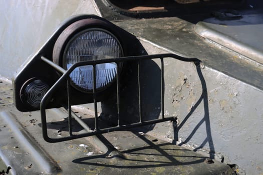 A high beam headlight protected by a special grille on old armored vehicles. Searchlight on military equipment.