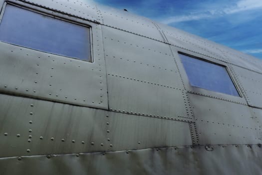 Airplane surface with two windows and illuminators, metal cladding with rivets, painted in green.