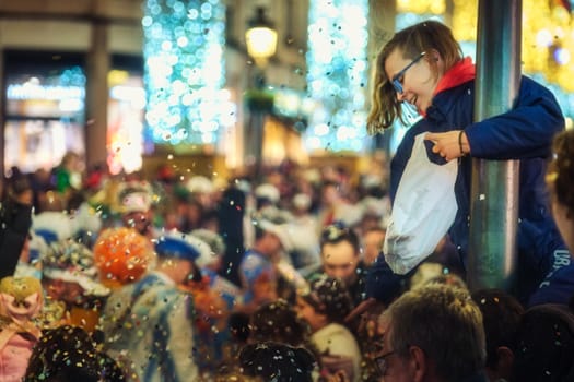 child with glasses holding onto what appears to be a pole or column. festive or celebratory atmosphere. The crowd engaged in some sort of activity that involves the tossing or releasing of these white specks.