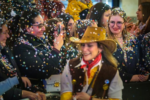 group of people in a festive environment. They appear to be enjoying themselves amidst a shower of colorful confetti, which adds to the joyful atmosphere. wearing costumes with a cowboy-themed style, such as hats and bandanas, event or celebration. The faces of the people indicate laughter and happiness