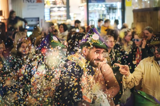 lively scene where people are celebrating, at a festival or carnival. They are wearing festive hats and costumes with a lot of colors and patterns. There are confetti in the air, a joyous event. people are smiling and appear to be having a great time.