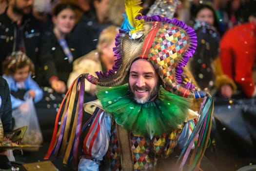 Festive celebrant in vibrant costume with geometric headdress enjoying confetti-filled carnival, amidst joyous spectators. High quality photo