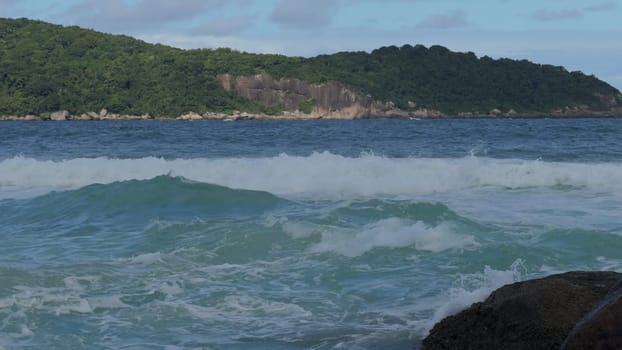 Slow-motion video captures powerful waves crashing onto a rocky coastline, surrounded by lush jungle.