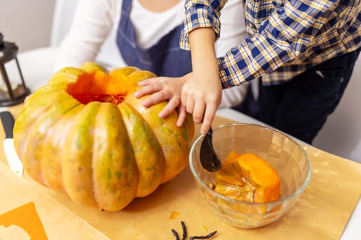 Child scooping out seeds from a large pumpkin with a spoon while preparing for Halloween. Close-up shot of hands working on pumpkin carving.