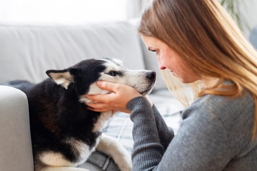 Woman gently holding her black and white dogs face, sitting on the couch, creating an intimate and tender moment. Indoor pet bonding scene.