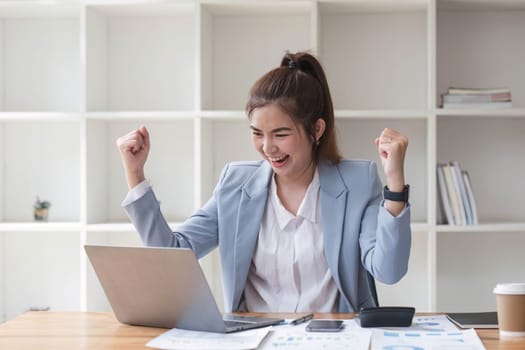 Asian businesswomen show joyful expression of success at work smiling happily with a laptop computer in a modern office..