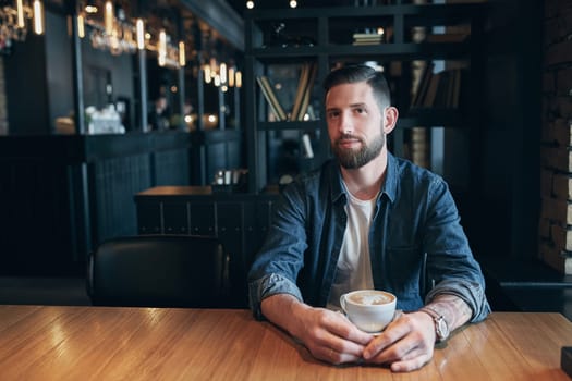 Confident man enjoying a cup of coffee while having work break lunch in modern restaurant, young intelligent man or entrepreneur relaxing in indoors cafe looking pensive