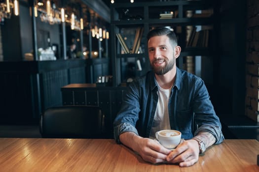 Confident man enjoying a cup of coffee while having work break lunch in modern restaurant, young intelligent man or entrepreneur relaxing in indoors cafe looking pensive