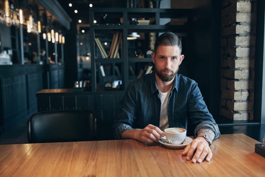 Confident man enjoying a cup of coffee while having work break lunch in modern restaurant, young intelligent man or entrepreneur relaxing in indoors cafe looking pensive