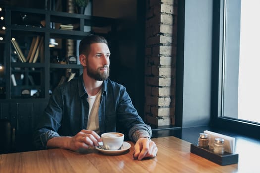 Confident man enjoying a cup of coffee while having work break lunch in modern restaurant, young intelligent man or entrepreneur relaxing in indoors cafe looking pensive