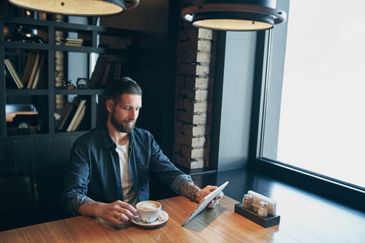 Young man drinking coffee in cafe and using tablet computer. Freelancer. Workplace. Lunch