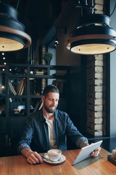 Young man drinking coffee in cafe and using tablet computer. Freelancer. Workplace. Lunch