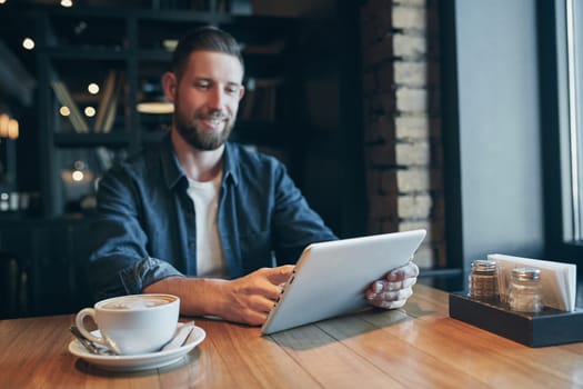 Young man drinking coffee in cafe and using tablet computer. Freelancer. Workplace. Lunch