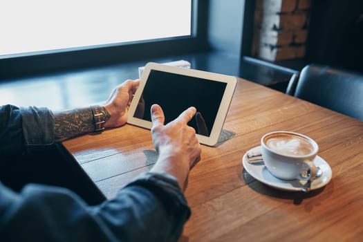 Close up hands man using tablet, connecting wifi. Working just from cafe. Young man in smart casual wear working on digital tablet while sitting near window. Black screen. Copy space