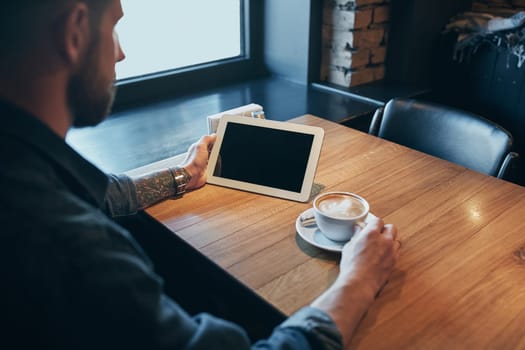 Close up hands man using tablet, connecting wifi. Working just from cafe. Young man in smart casual wear working on digital tablet while sitting near window. Black screen. Copy space