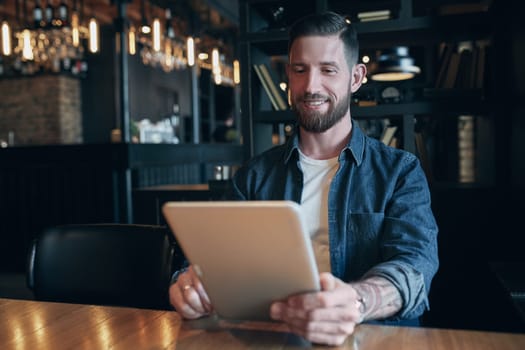 Modern hipster businessman drinking coffee in the city cafe during lunch time and working on tablet. Freelancer