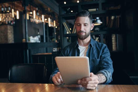 Modern hipster businessman drinking coffee in the city cafe during lunch time and working on tablet. Freelancer