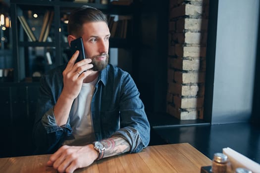 Talking with friends. Confident young man talking on the mobile phone and smiling while sitting in cafe