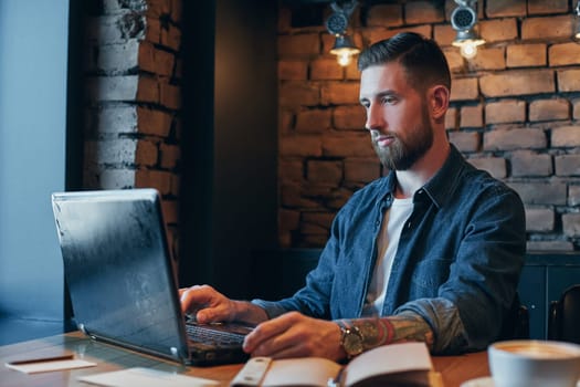 No minute without my laptop. Handsome young man working on laptop while enjoying coffee in cafe.