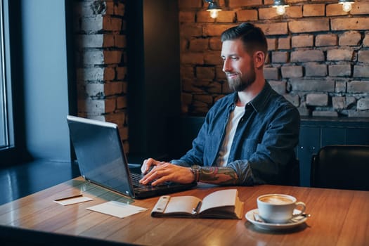 No minute without my laptop. Handsome young man working on laptop while enjoying coffee in cafe.