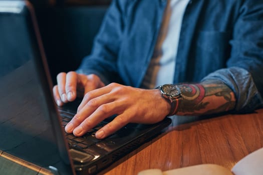 Young hipster guy at the bar having a cappuccino. Young man drinking coffee in city cafe during lunch time and working on laptop. Close up