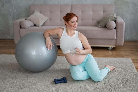 Pregnant woman drinks water after workout on fitness ball