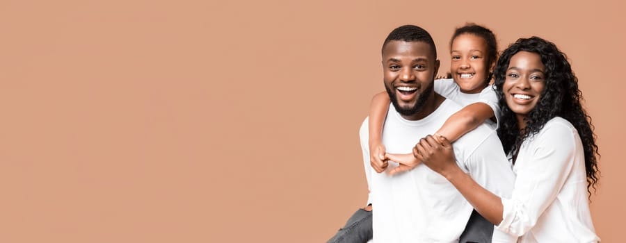 Family fun. Young african american parents spending time with their little daughter, laughing together over yellow background