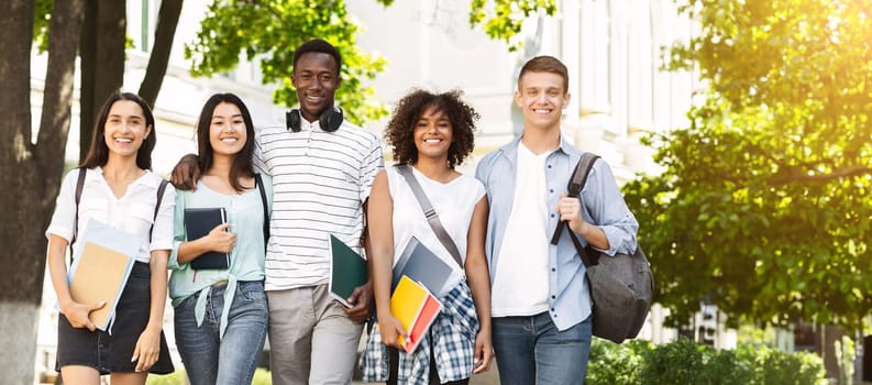 Cheerful college students walking out of campus together, and posing at camera outdoors, having break in classes, free space
