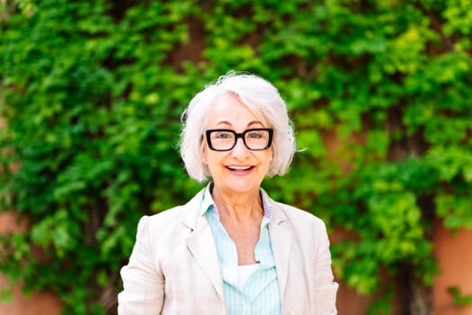 portrait of a middle age woman smiling happy looking at camera with blurred green plants background, concept of mature people lifestyle