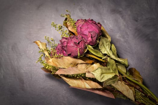 A studio photo of a bouquet of dried red roses on a table.