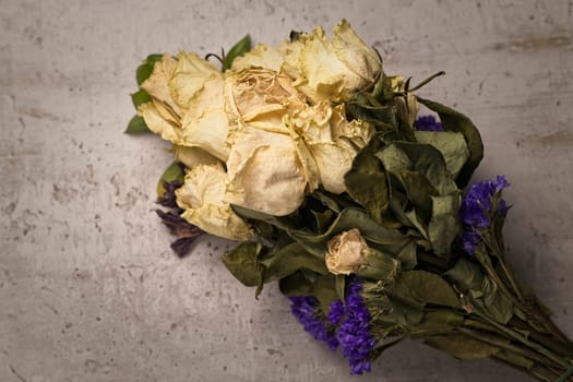A studio photo of a bouquet of dried yellow roses on a table.