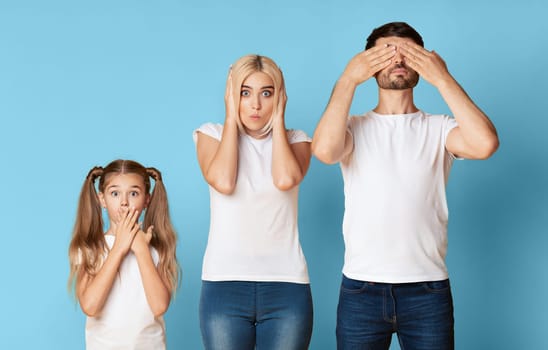 A family of three stands in front of a blue background. The father has his hands over his eyes, the mother has her hands over her ears, and the young daughter has her hands over her mouth